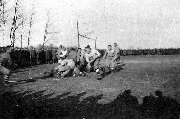 From my uncle’s WWI photo album, this photo shows the gridiron surrounded by soldiers in full uniform. The action on the field is quite compelling as the ball carrier runs to the left for the goal line. Note the makeshift goal post in the background.