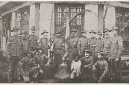 The American survivors of the attack pose with one of the captured church bells used by Filipino insurgents to coordinate the attack against the Americans.