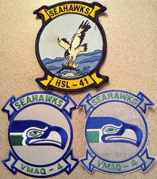 These patches represent two squadrons – one a USMC electronic warfare squadron and the other, an anti-submarine warfare helicopter squadron. Both bear the same nickname of “Seahawks.” The bottom two patches’ design was incorporated into the Marine Tactical Electronic Warfare Squadron (#4) when it was based at NAS Whibey Island in Washington State. The Seahawks (squadron) adopted the imagery from the Seahawks (the local NFL team). Since relocating to Marine Corps Air Station Cherry Point, VMAQ-4 departed from the NFL-based design,